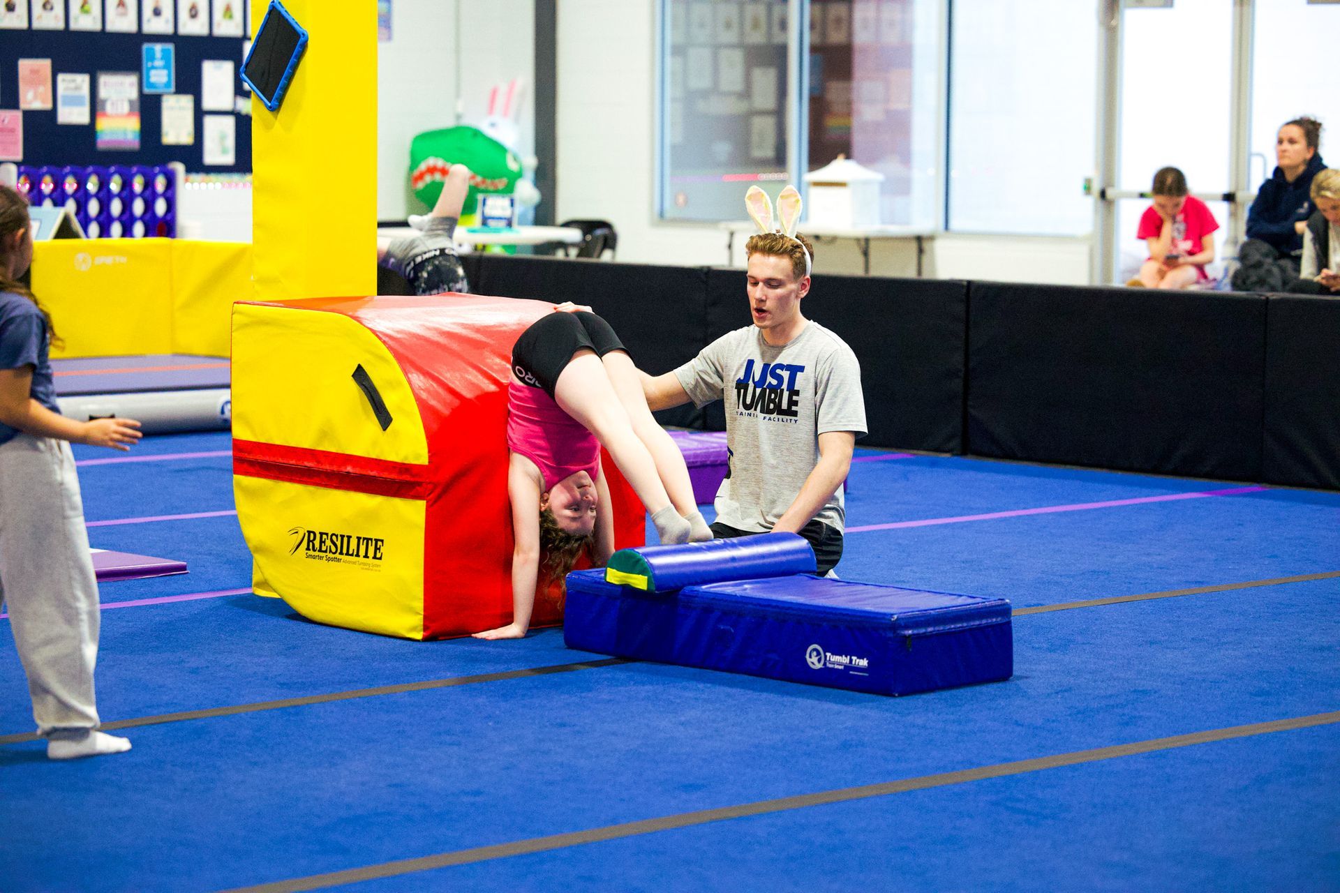 Girl in green shirt doing the splits on a blue mat, smiling.