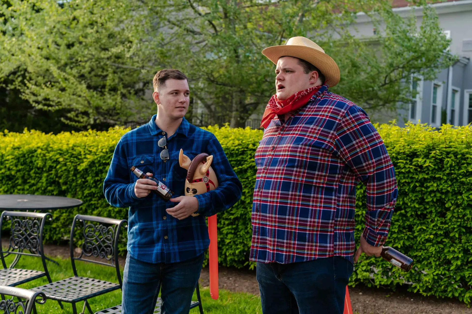 A man in a cowboy hat is standing next to another man in a plaid shirt.