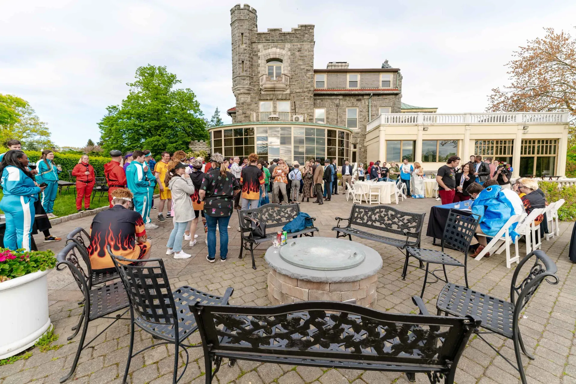 A group of people are standing around a fire pit in front of a castle.