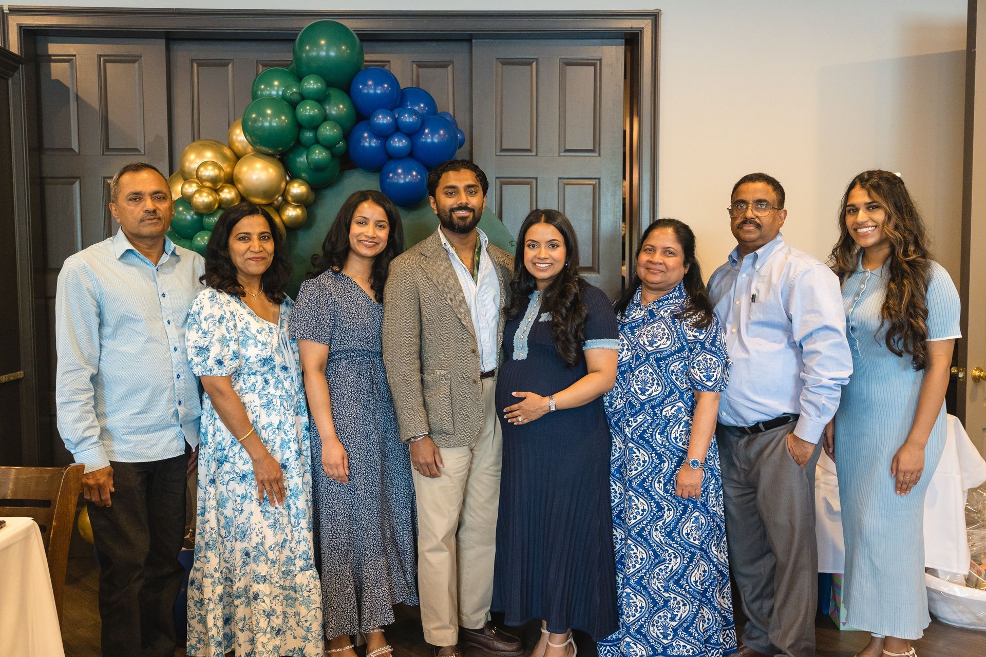 Group portrait of seven people in front of a gold and green balloon arch indoors