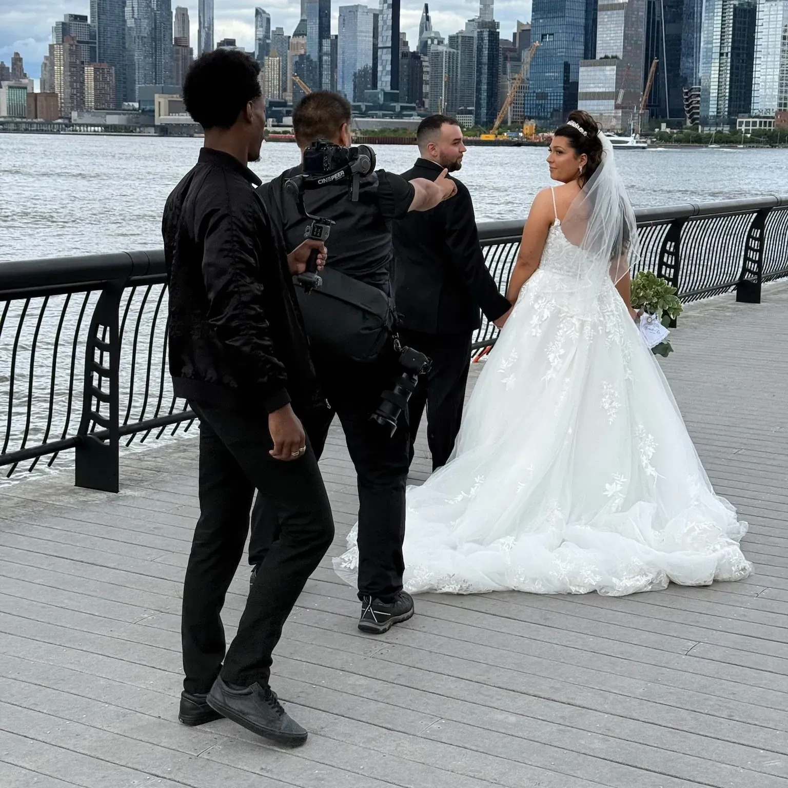 Wedding couple posing on a waterfront promenade with a city skyline in the background.