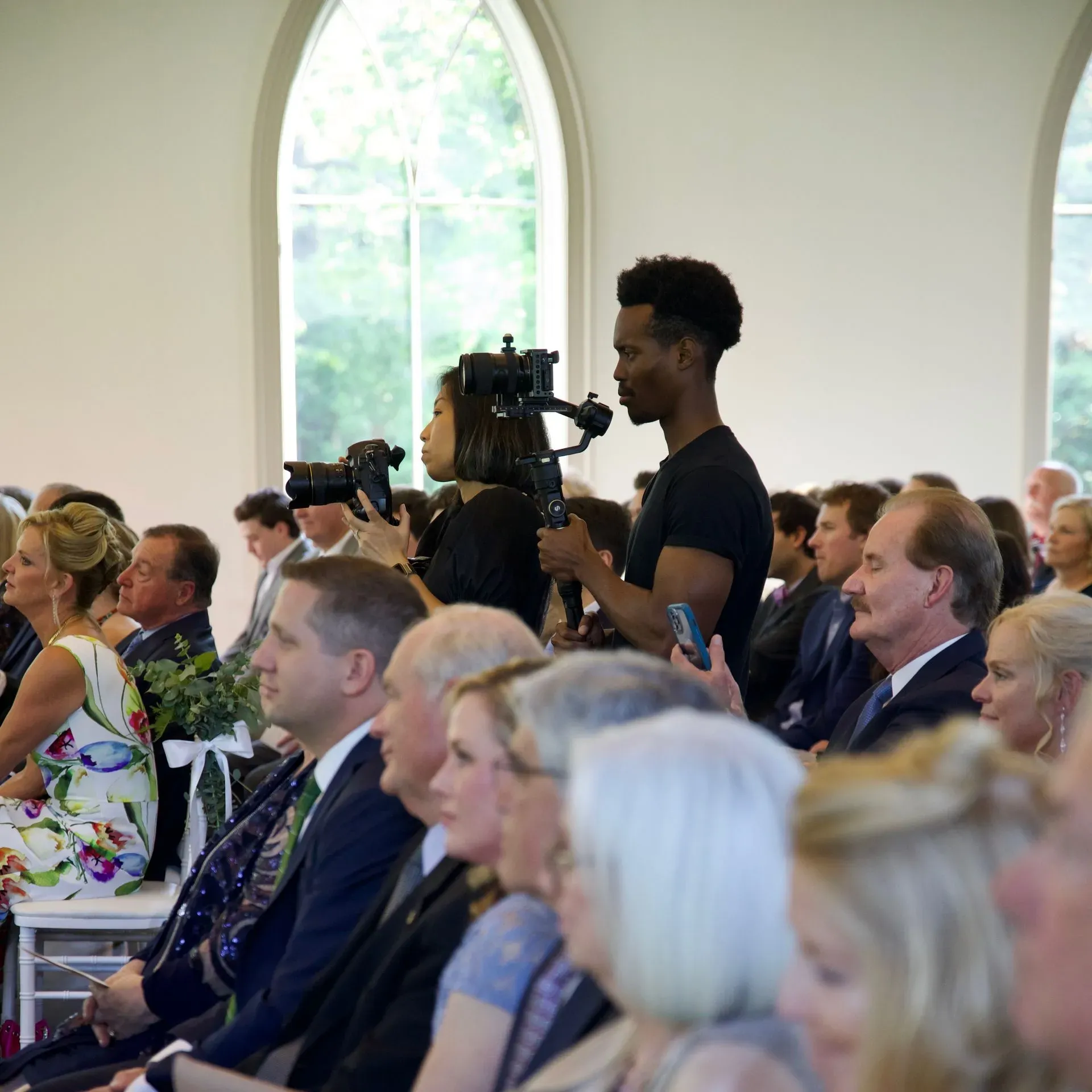 Audience at a formal event; a cameraman films from the aisle beside seated guests.