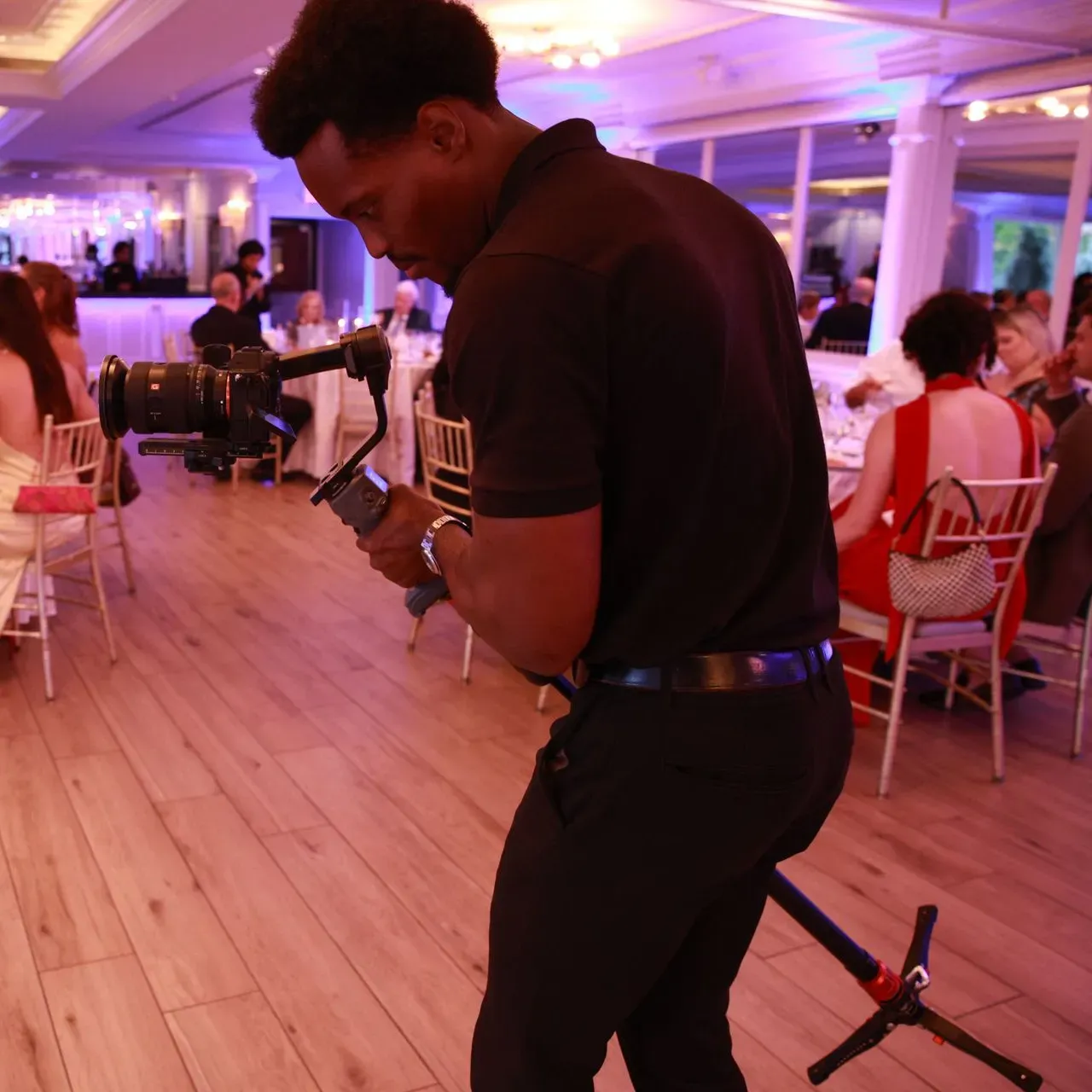 Photographer adjusting a camera in a pink-lit banquet hall with guests seated at tables