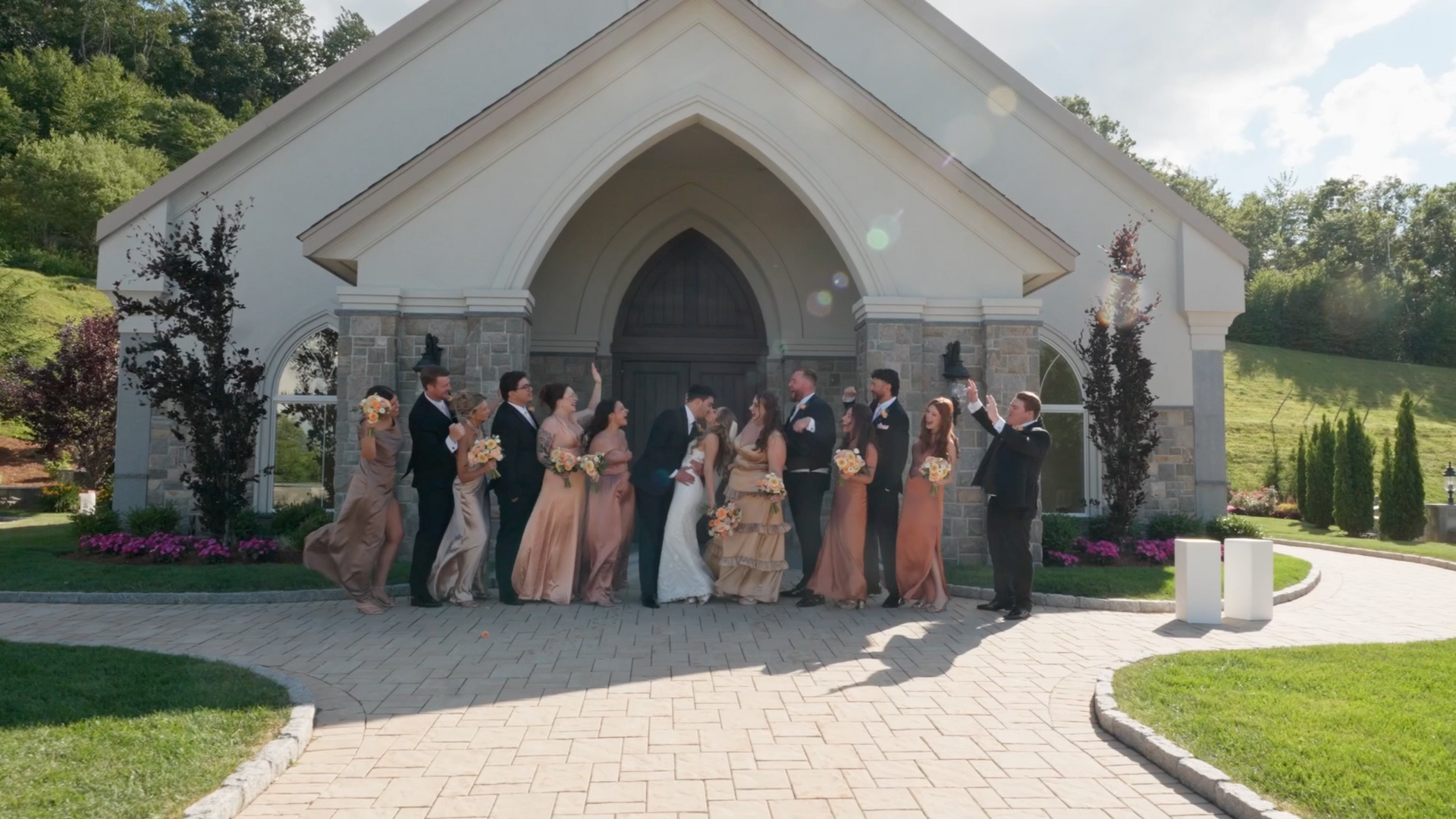 Newlyweds kiss as their wedding party cheers outside the chapel at Aria Wedding & Banquet Facility