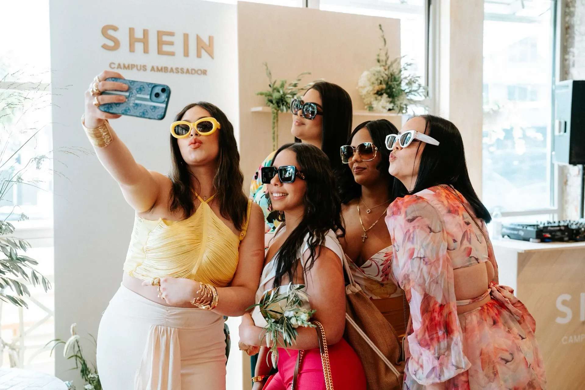 A group of women are taking a selfie together in front of a shein sign.