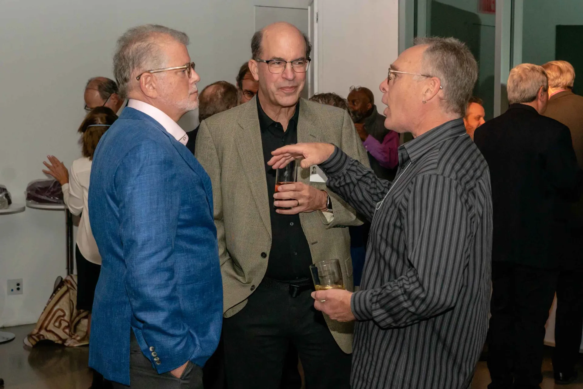 A group of men are standing in a room talking to each other.