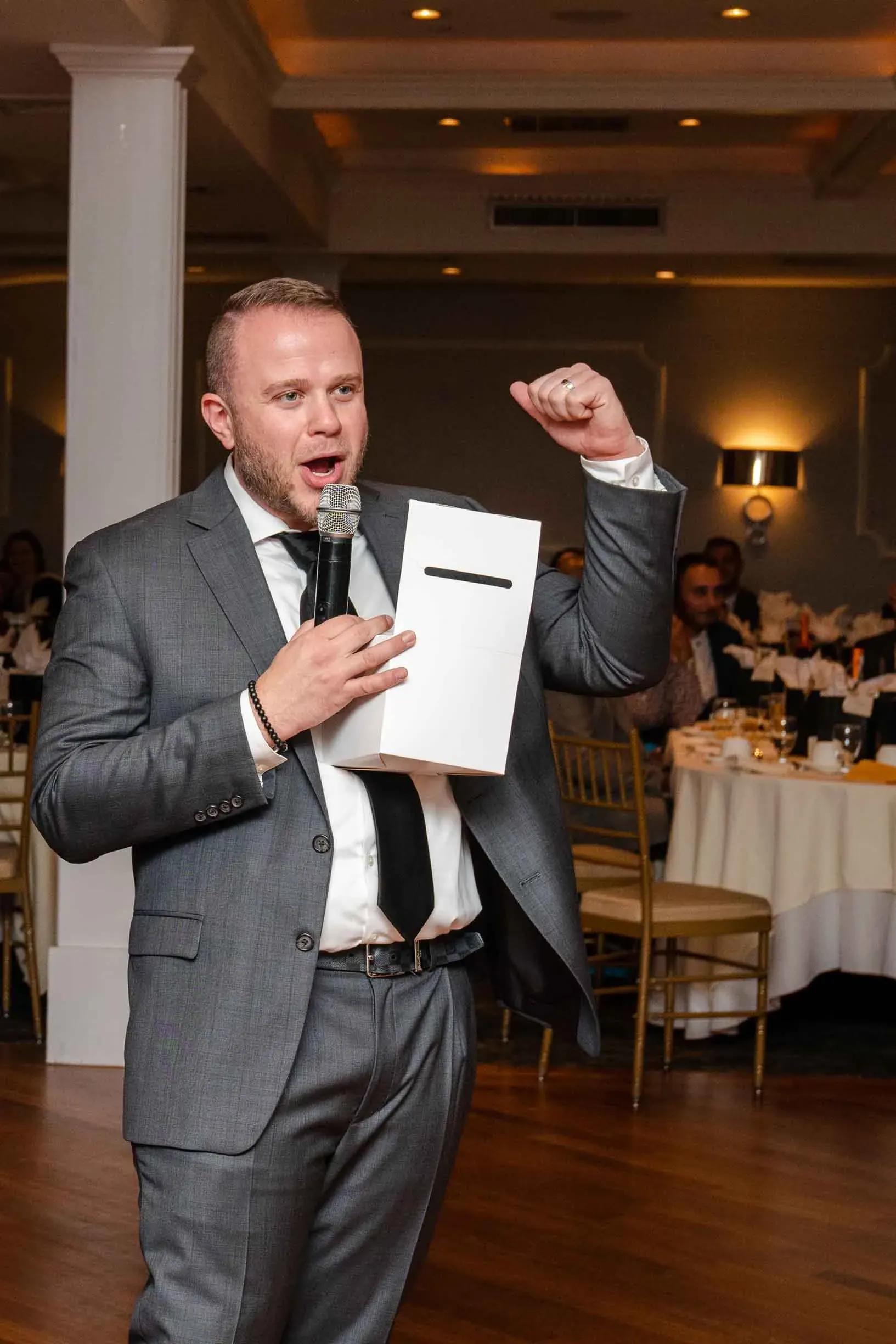 A man in a suit and tie is holding a microphone and giving a speech.