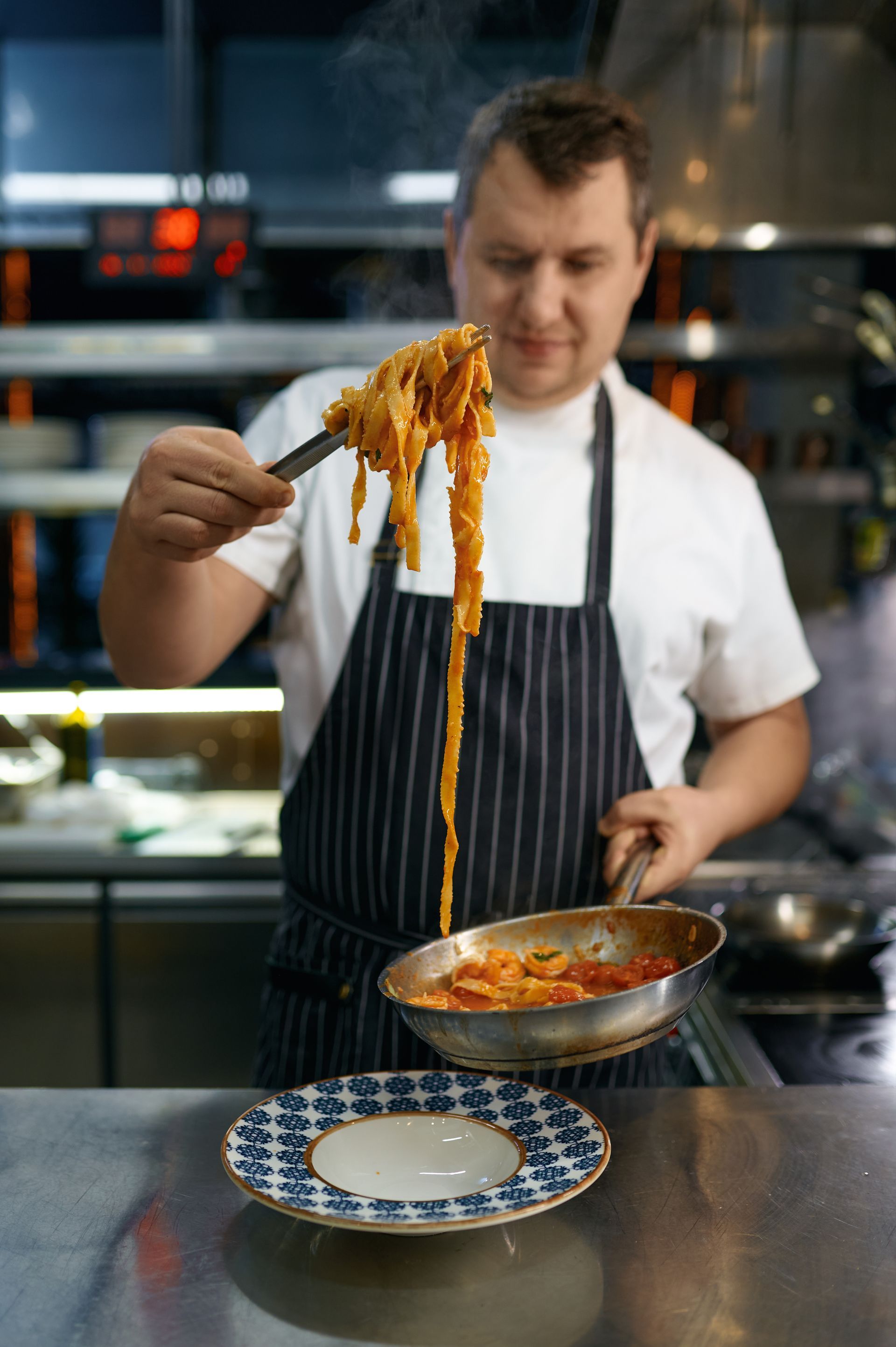 A man is cooking spaghetti in a pan in a kitchen.