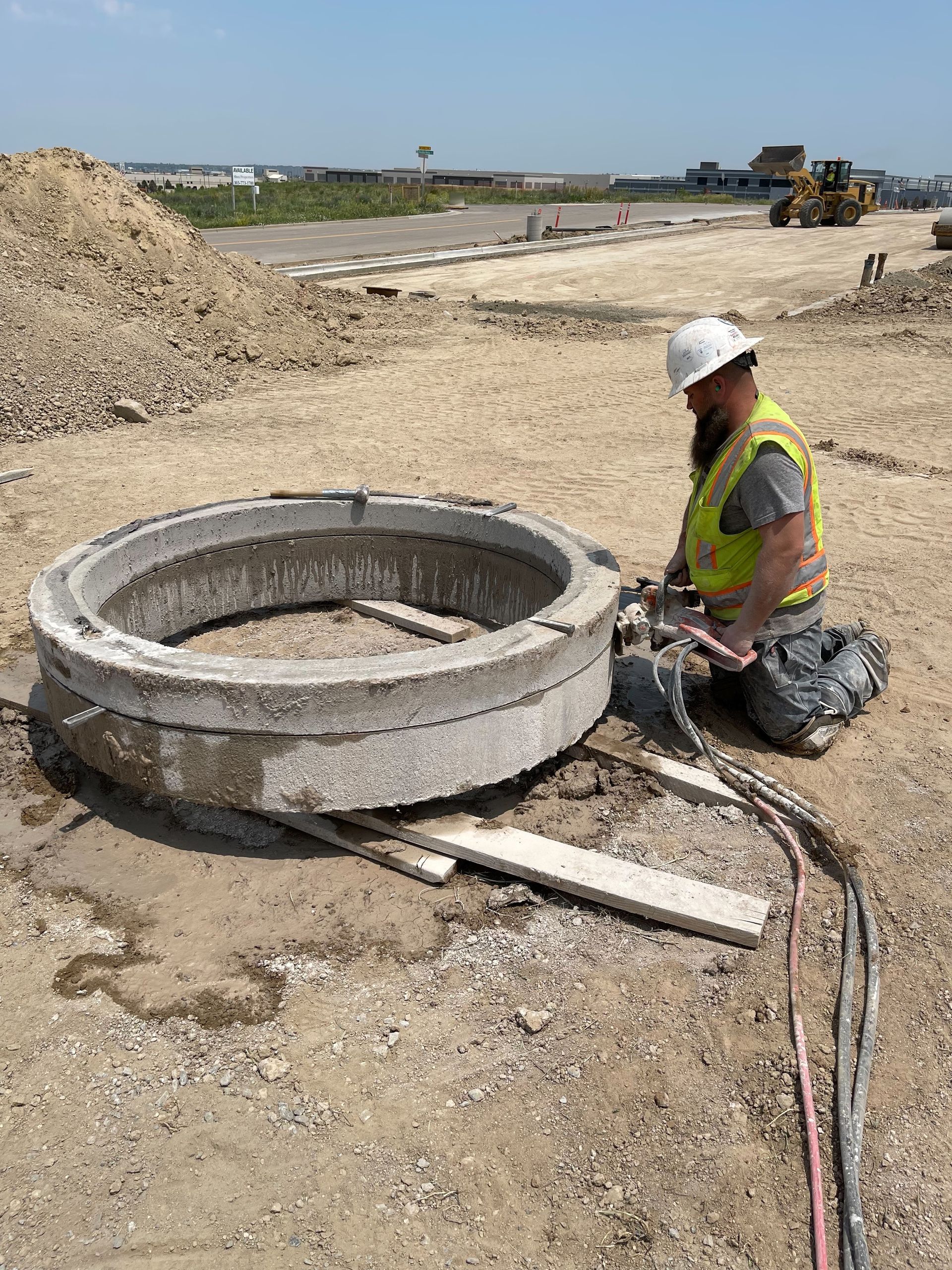 Construction worker in jeans and work boots using a concrete saw on pavement, creating a dust cloud.
