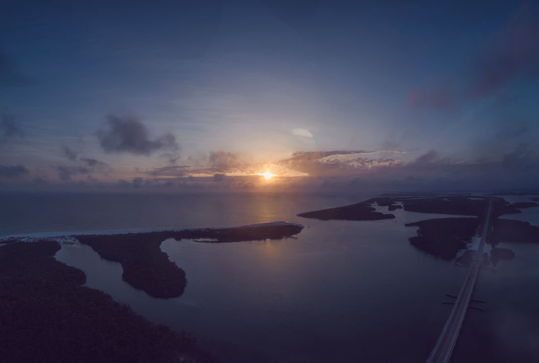 Sunset over calm water with small islands and a long bridge stretching into the distance