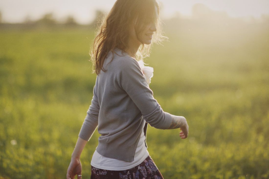 Person walking through a sunlit grassy field at golden hour