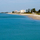 Turquoise ocean beside a sandy beach with distant buildings under a clear sky