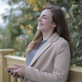 Woman standing by a yellow railing outdoors, smiling and holding a phone.
