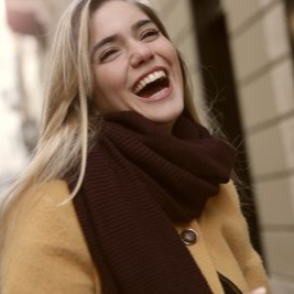 Smiling woman in a mustard coat and brown scarf on a city street