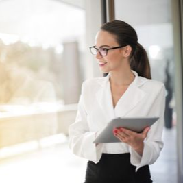 Professional woman in a white blazer holding a tablet in a bright office hallway