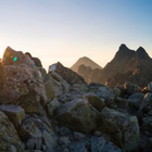Hiker standing on rocky mountain summit at sunrise, silhouetted against bright sky.