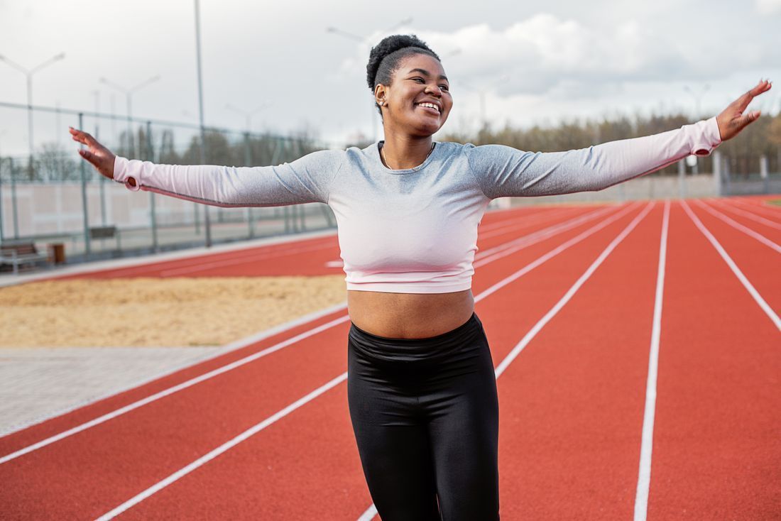 Woman smiling with arms outstretched on a red running tracke