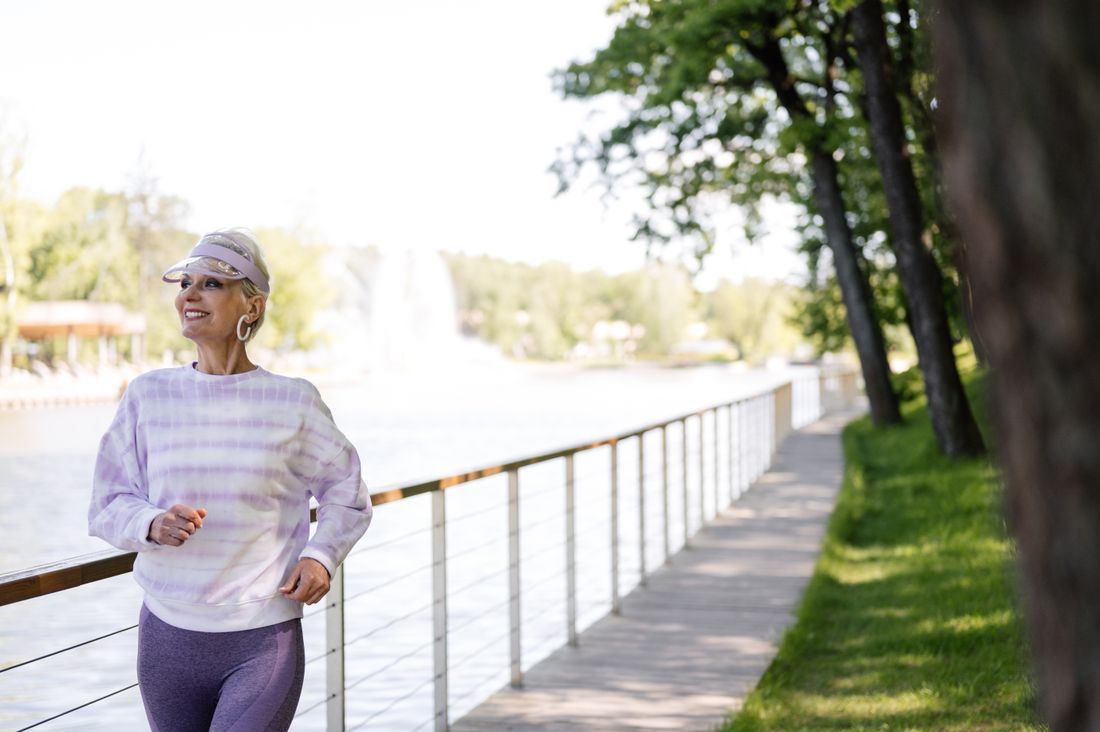 Woman jogging along a riverside path beside a railing and trees on a sunny day