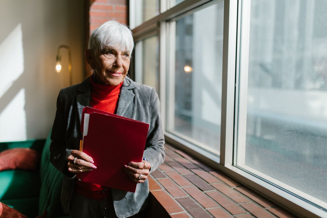 Woman holding a red folder in a bright hallway with large windows