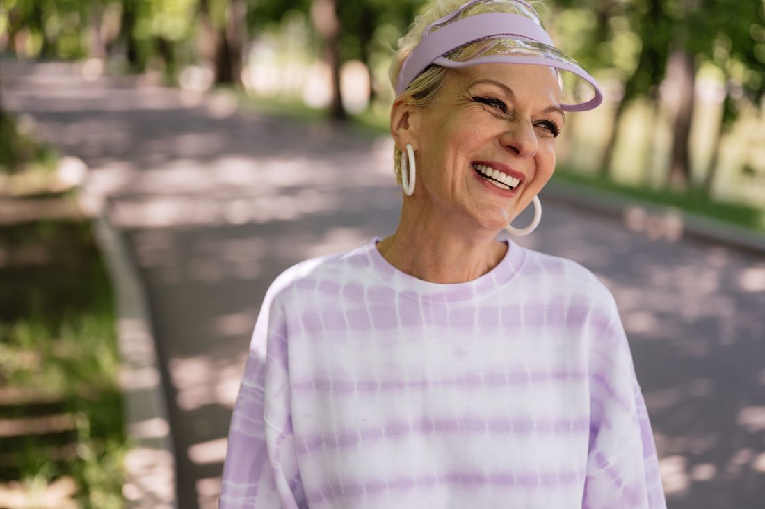 Smiling woman in a light striped shirt and visor standing on a tree-lined path