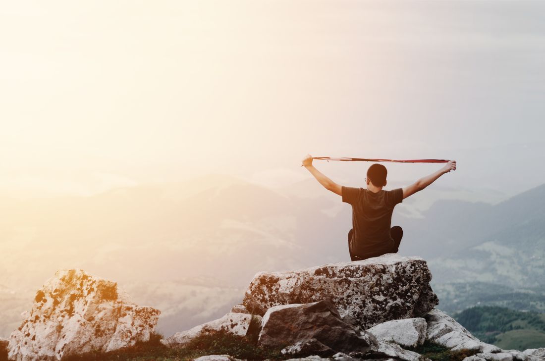 Person standing on a snowy mountain peak at sunrise with arms raised toward the sky