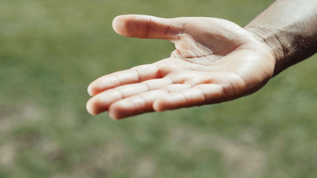 Open palm of a hand reaching out against a blurred green background