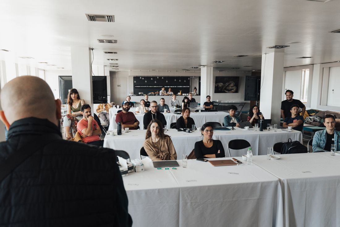 Audience seated in a bright conference room, listening to a speaker at the front