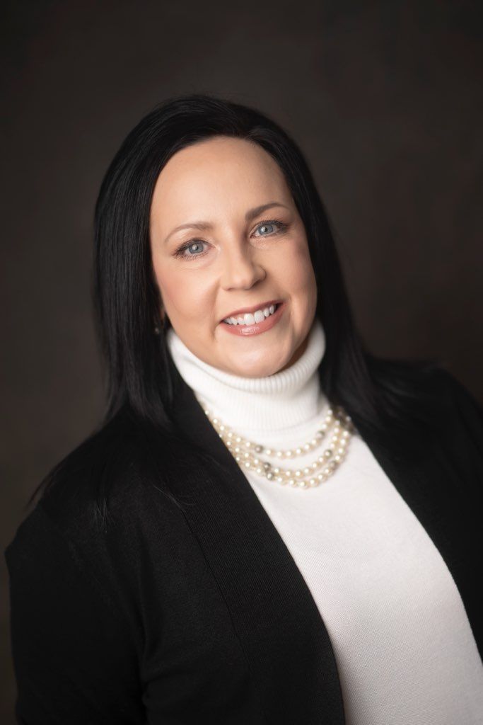 Portrait of a smiling woman in a black jacket and white turtleneck against a dark background