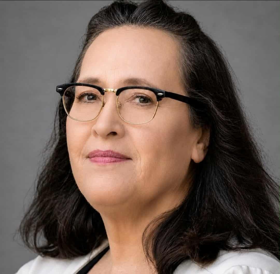 Close-up portrait of a person wearing black glasses, with dark hair and a slight smile on a gray background
