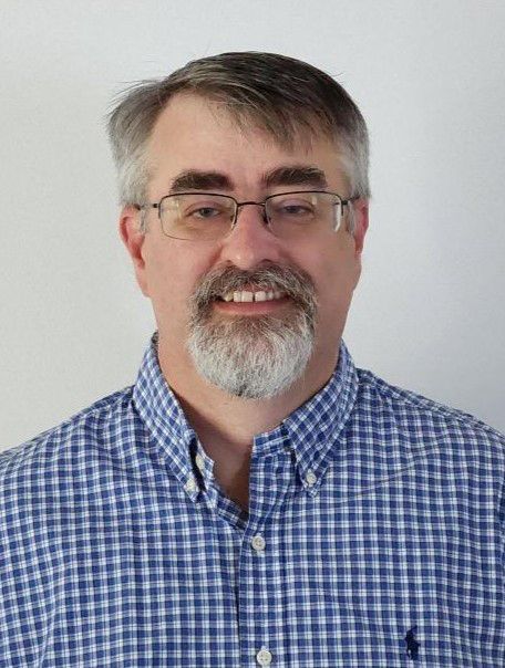 Head-and-shoulders portrait of a smiling man in glasses and a blue checkered shirt