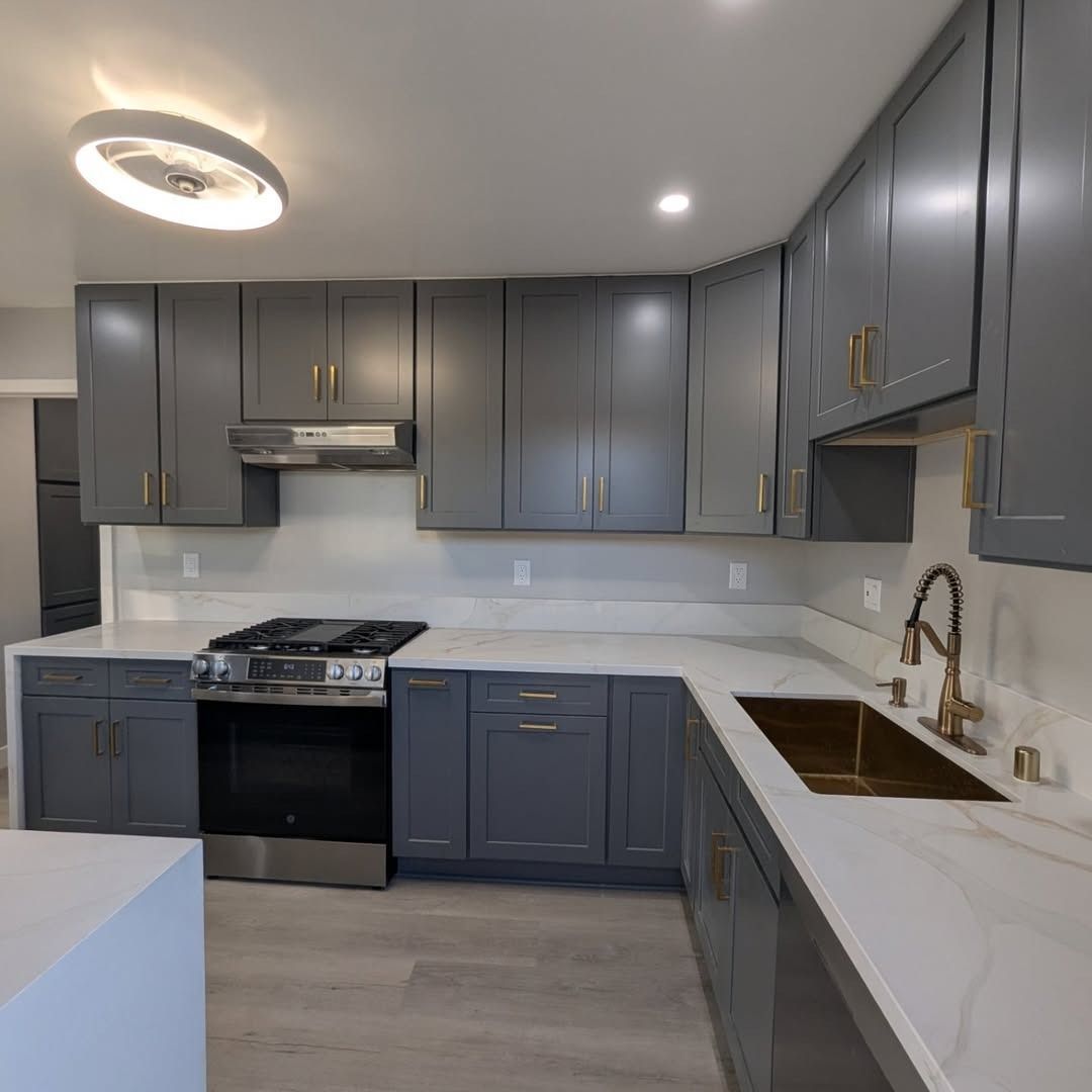 Modern kitchen with dark gray cabinets, white countertops, stainless stove, and brass faucet