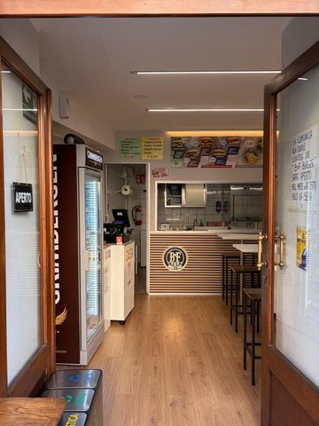Ingresso stretto di un ristorante, con pavimento in legno, bancone sul fondo e sgabelli lungo la parete destra.