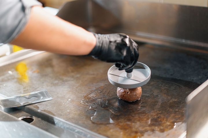 Mano guantata che usa una spatola per pulire una piastra rovente in cucina