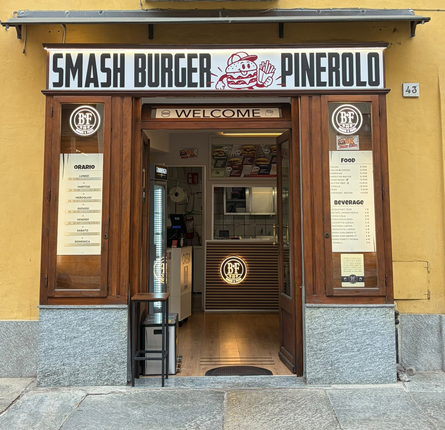 Ingresso aperto di un ristorante, con luci calde, porta in legno e la scritta “WELCOME” sopra la porta.