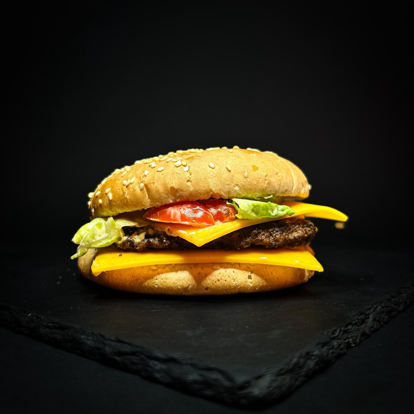 Hamburger al sesamo con formaggio, pomodoro e lattuga su uno sfondo scuro