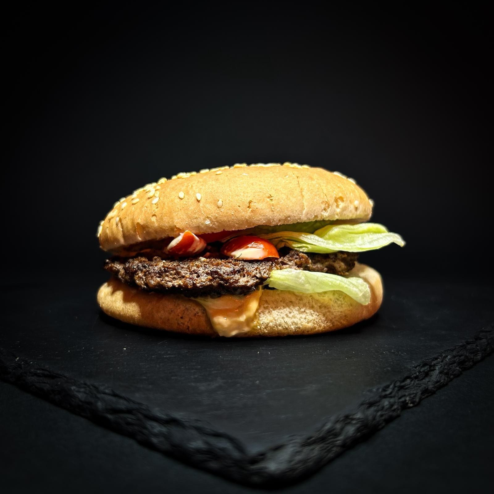 Hamburger al sesamo con lattuga e pomodoro su un piatto di ardesia scura, su sfondo nero