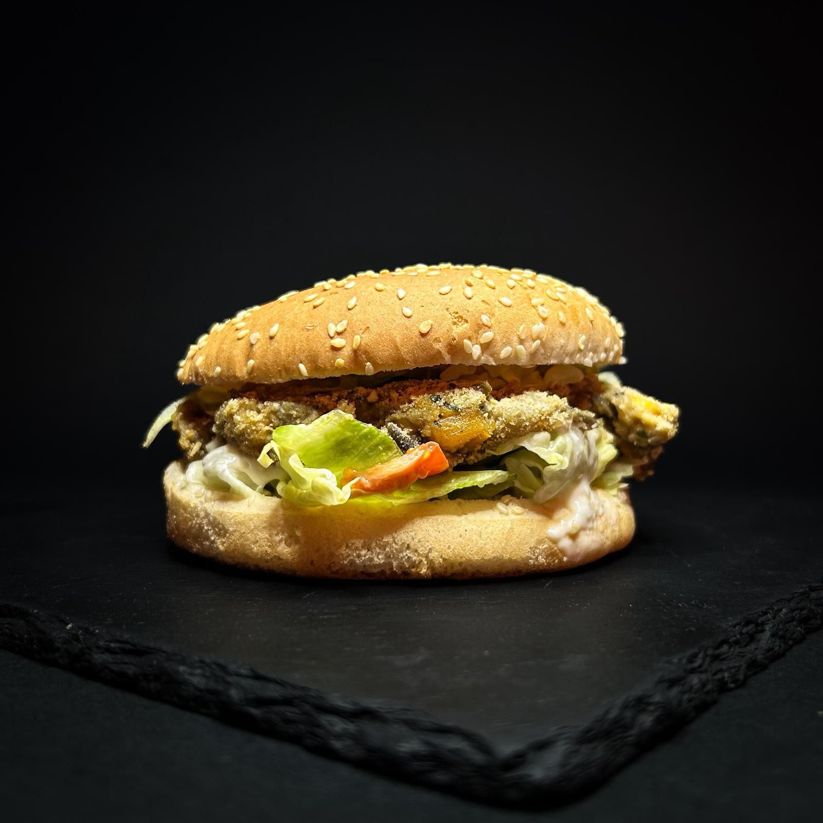 Hamburger al sesamo con lattuga e salsa su uno sfondo di ardesia scura