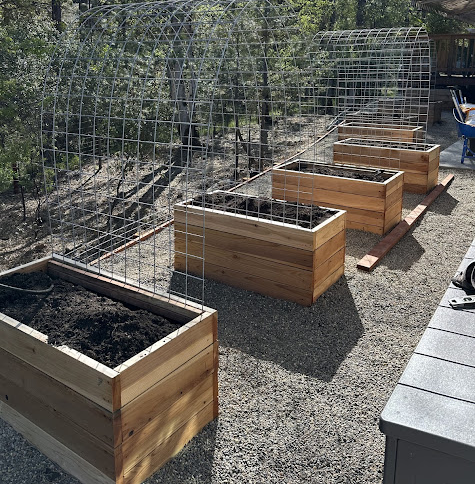 A row of wooden planters filled with dirt and a fence in the background.