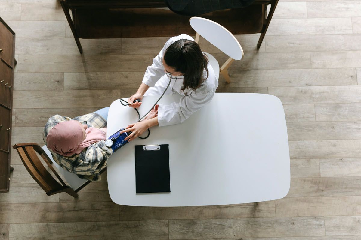 A doctor in a white coat measures a patient's blood pressure at a clinic.