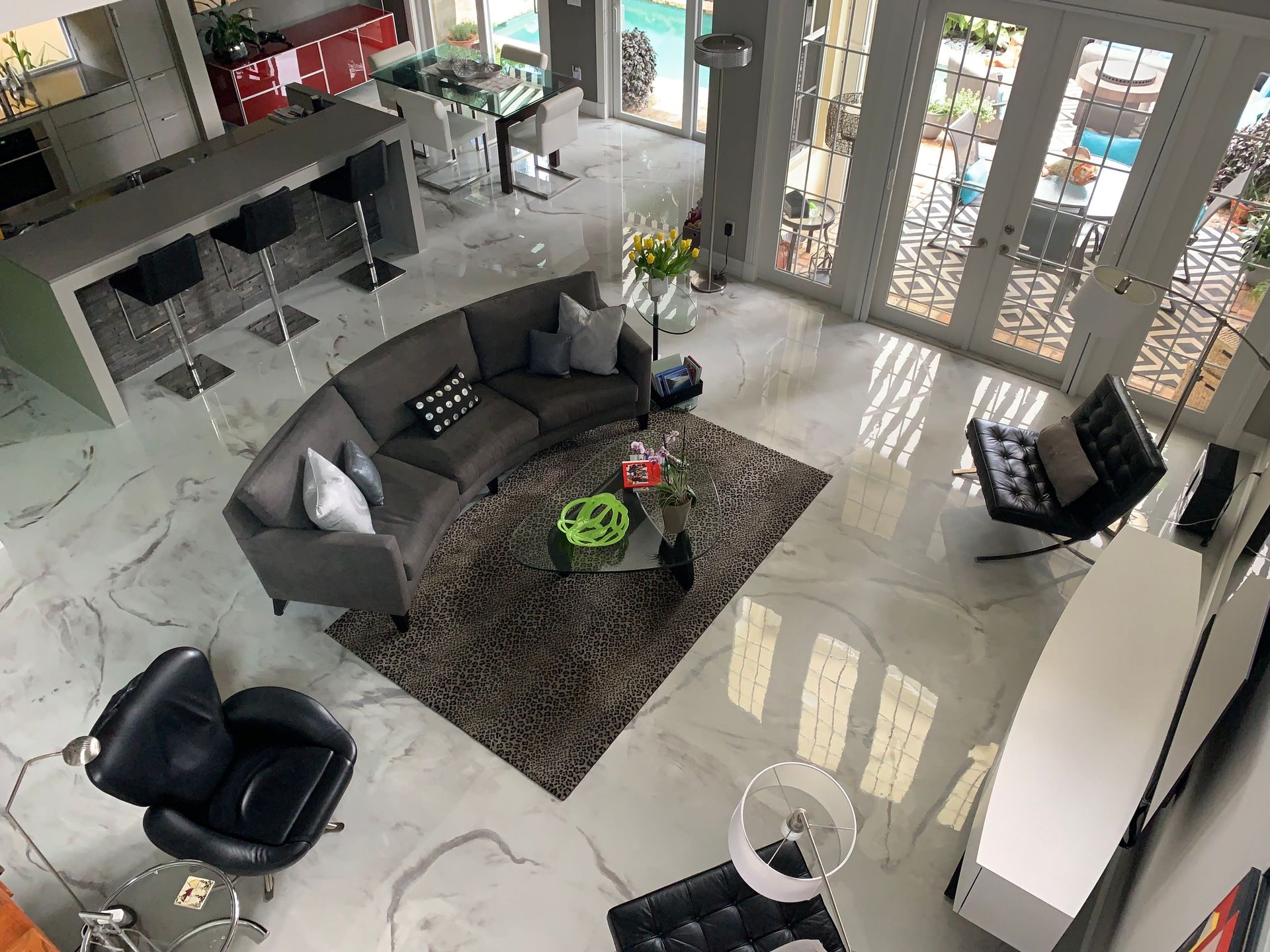 High-angle view of a modern living room with gray sofa, marble floors, and doors leading to a pool.