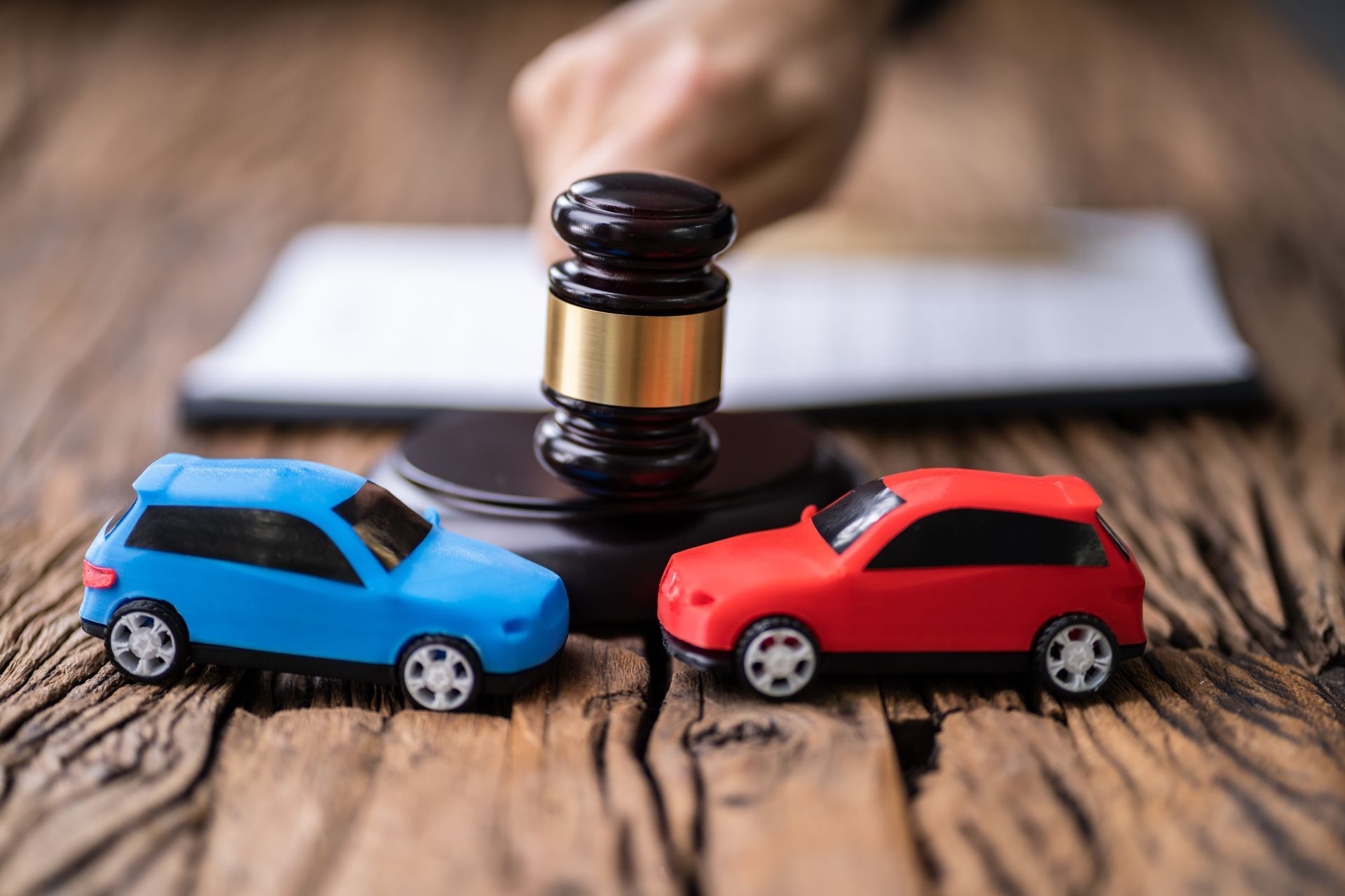Toy blue and red cars facing a judge’s gavel on a wooden desk, symbolizing an auto accident claim