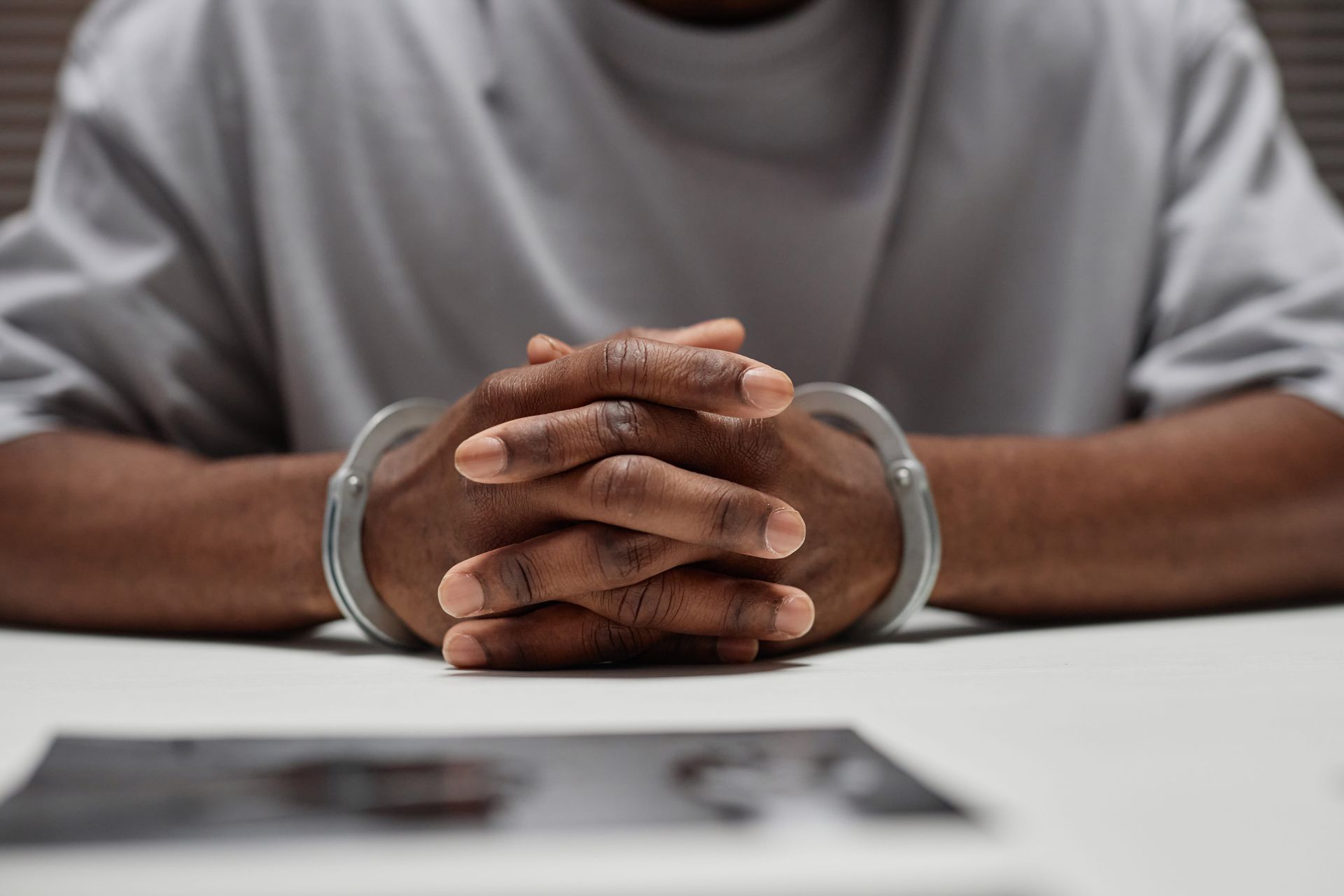 Handcuffed person in gray shirt with clasped hands on a table during an interview or arrest.