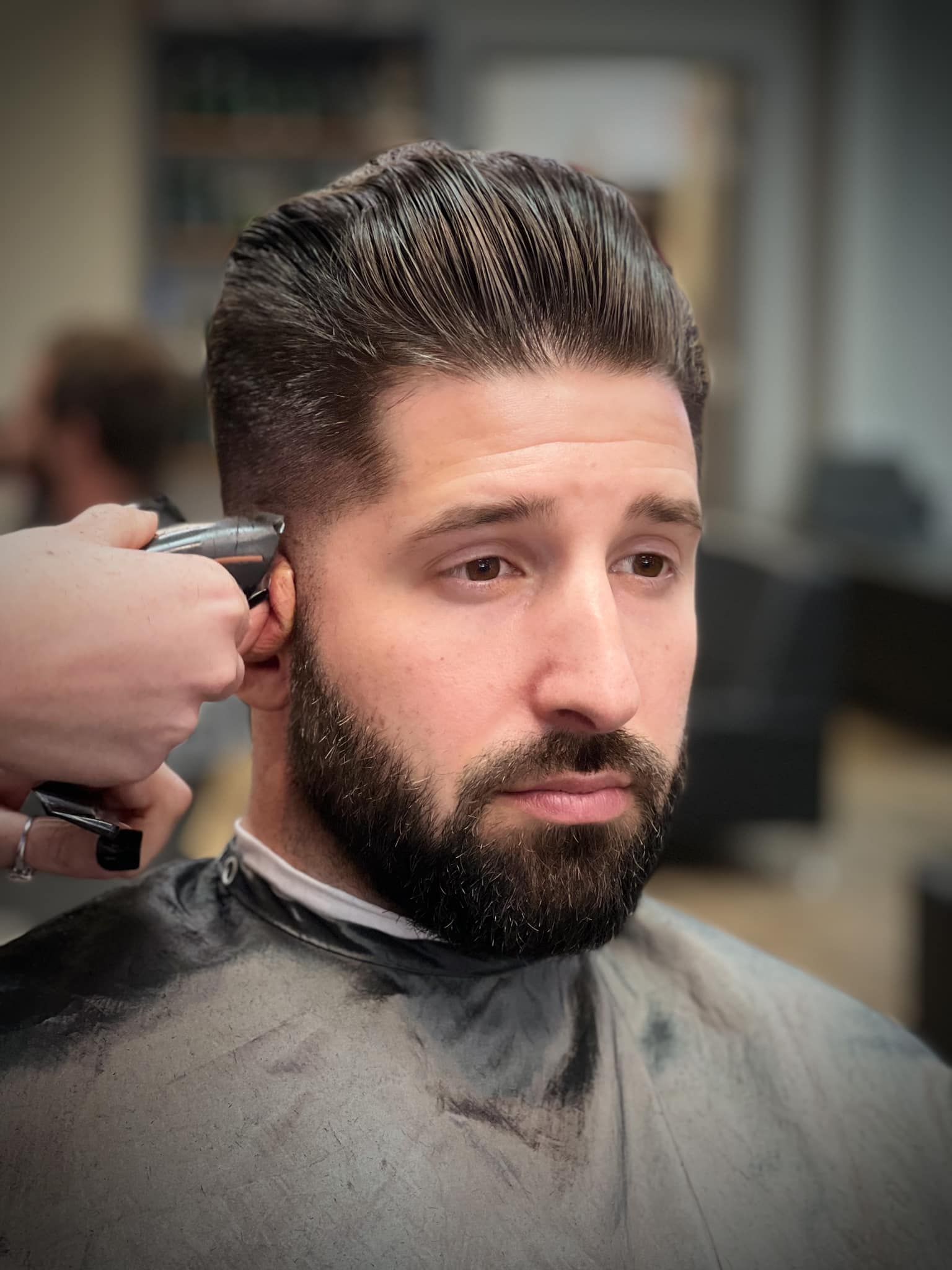 Barber trimming a man’s hair and beard with clippers in a salon chair