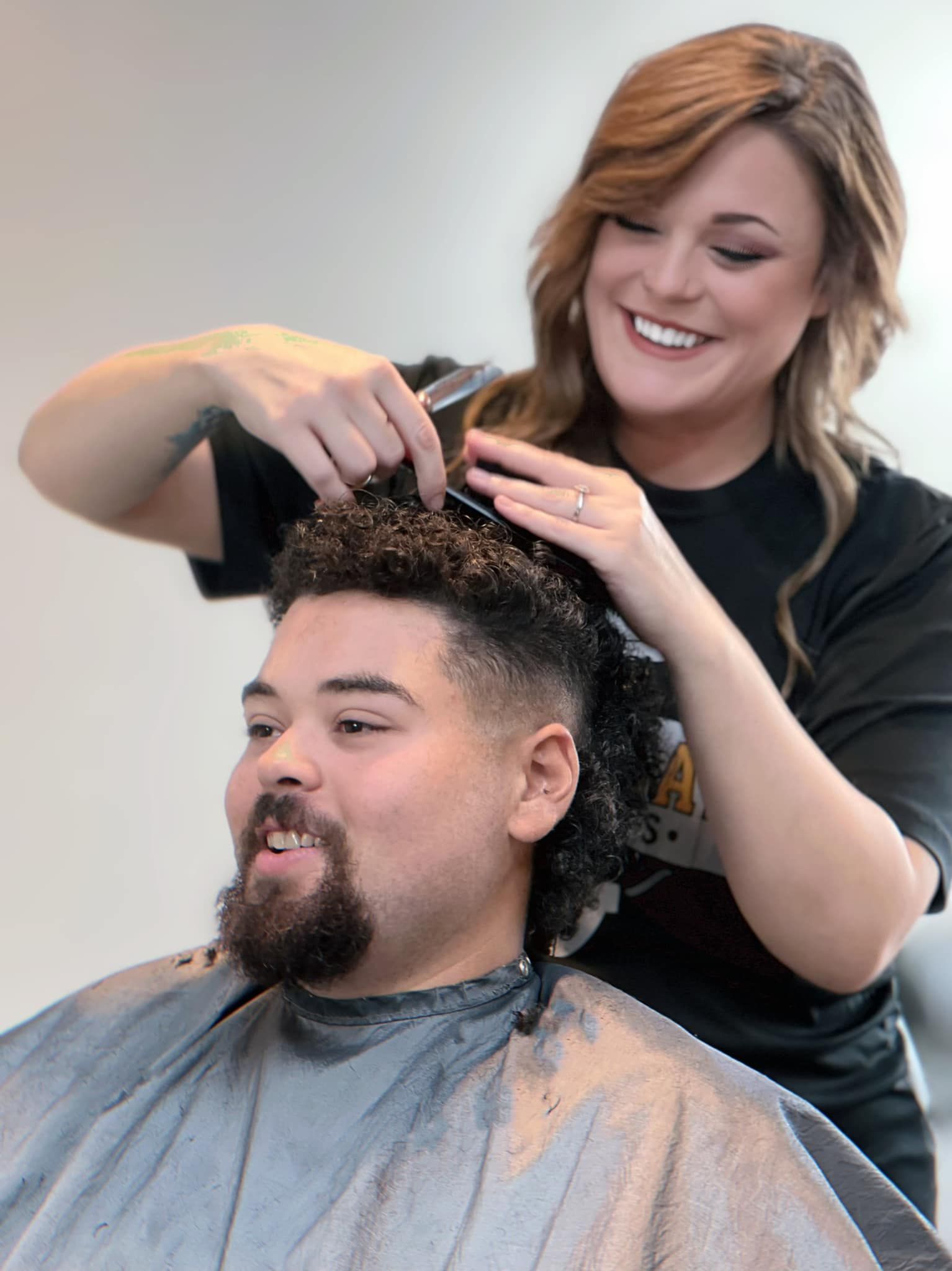 Hairdresser styling a smiling client’s curly hair in a salon