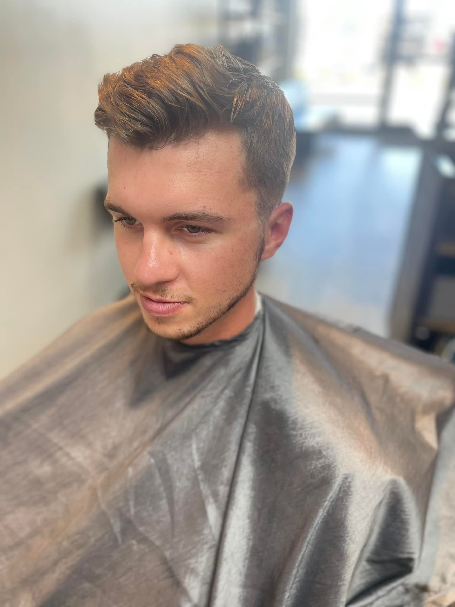 Man in a salon cape with short styled hair, looking down in a barbershop chair.