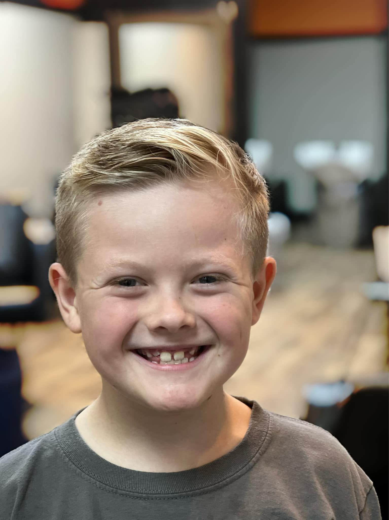 Smiling child in a gray shirt standing indoors with a blurred background