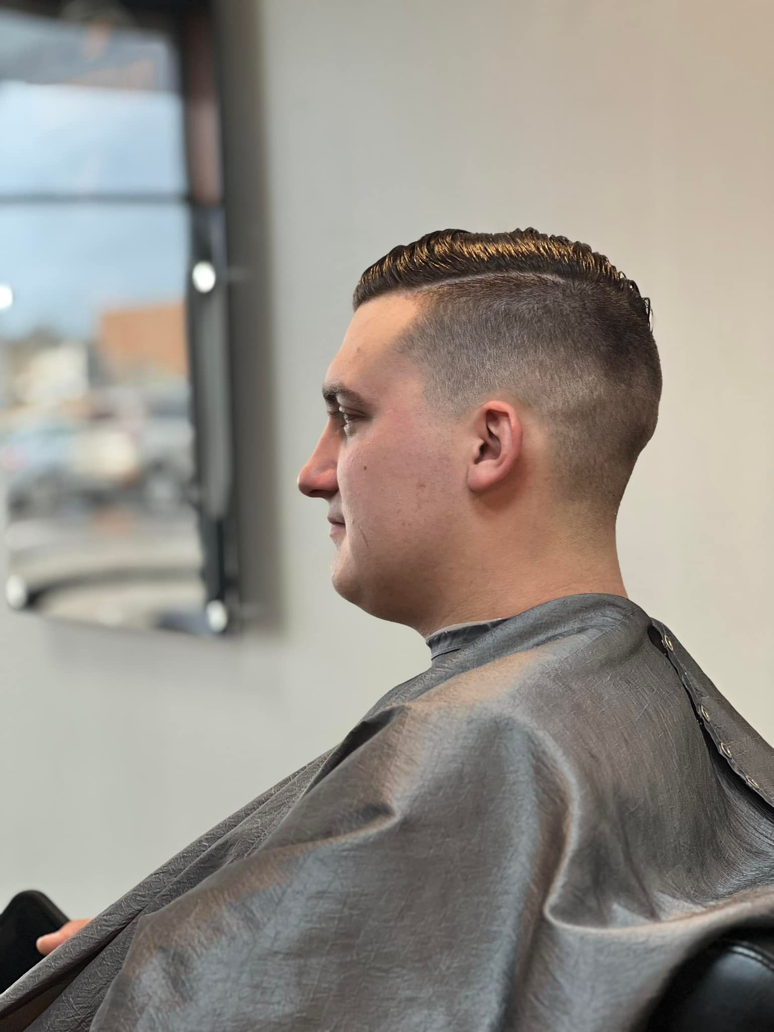 Side profile of a person getting a haircut in a barbershop, wearing a gray cape.