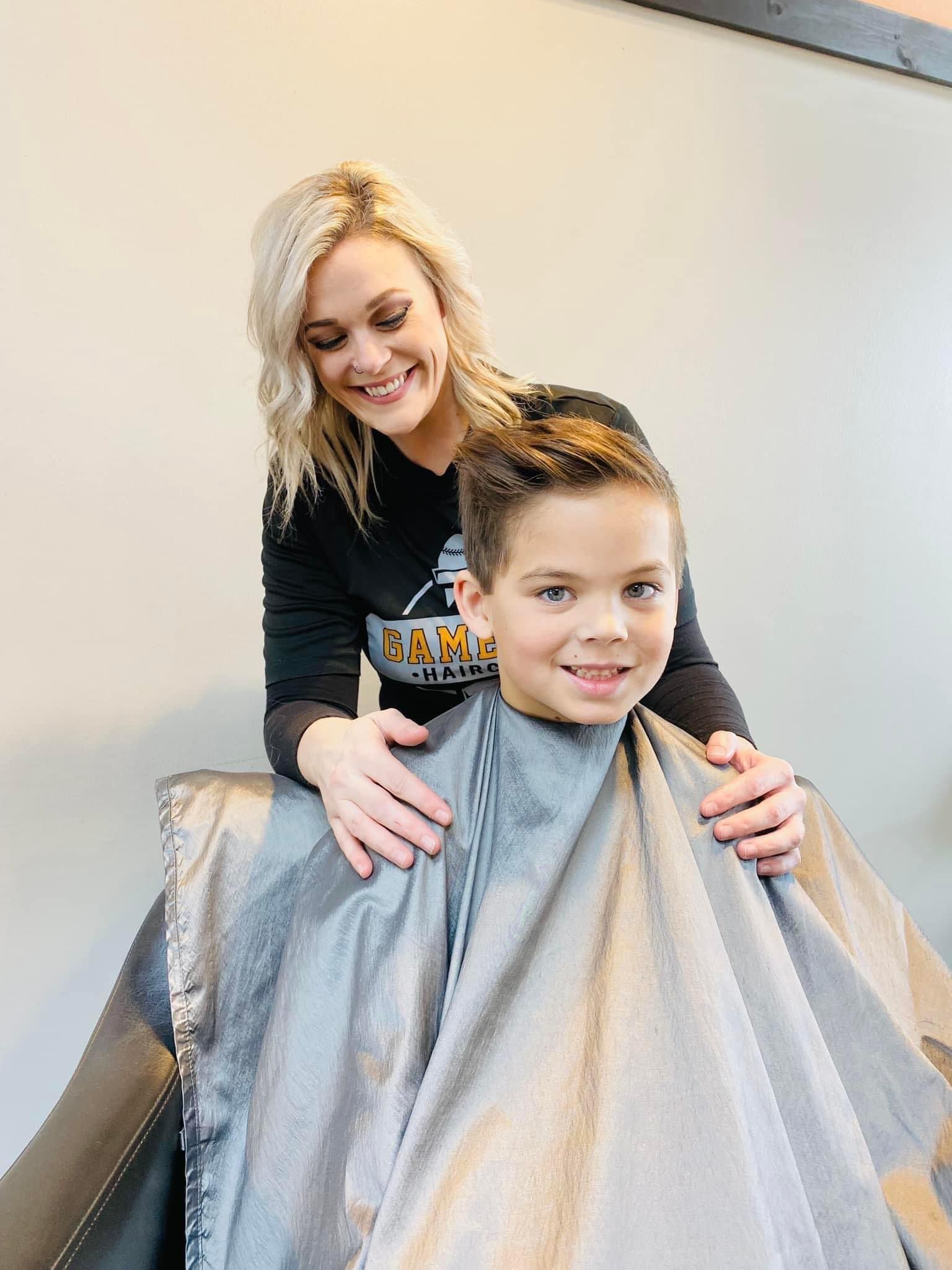 Hairdresser smiling behind a child in a salon cape, styling their hair.