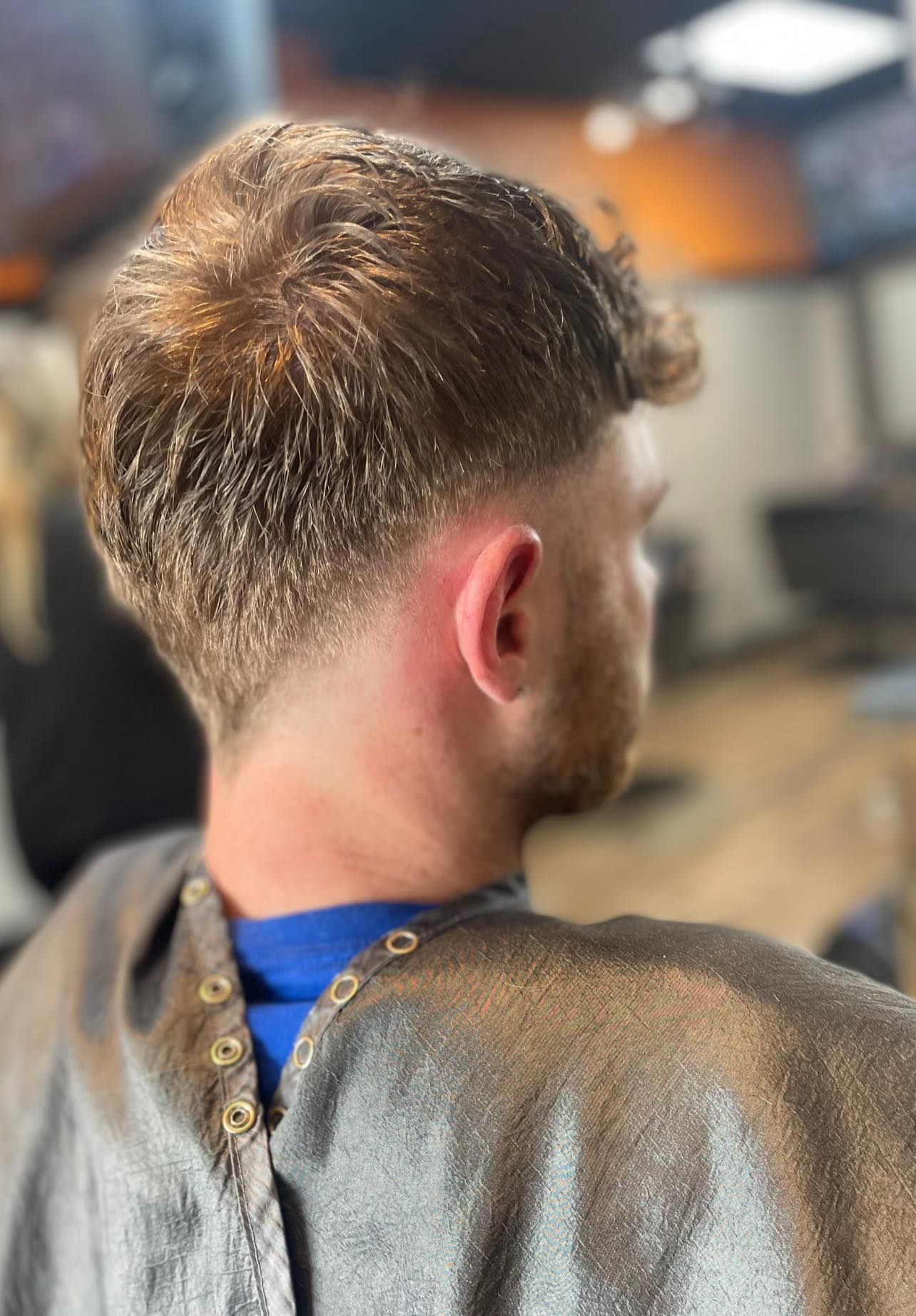 Person with short faded haircut shown from behind in a salon chair, wearing a gray cape.