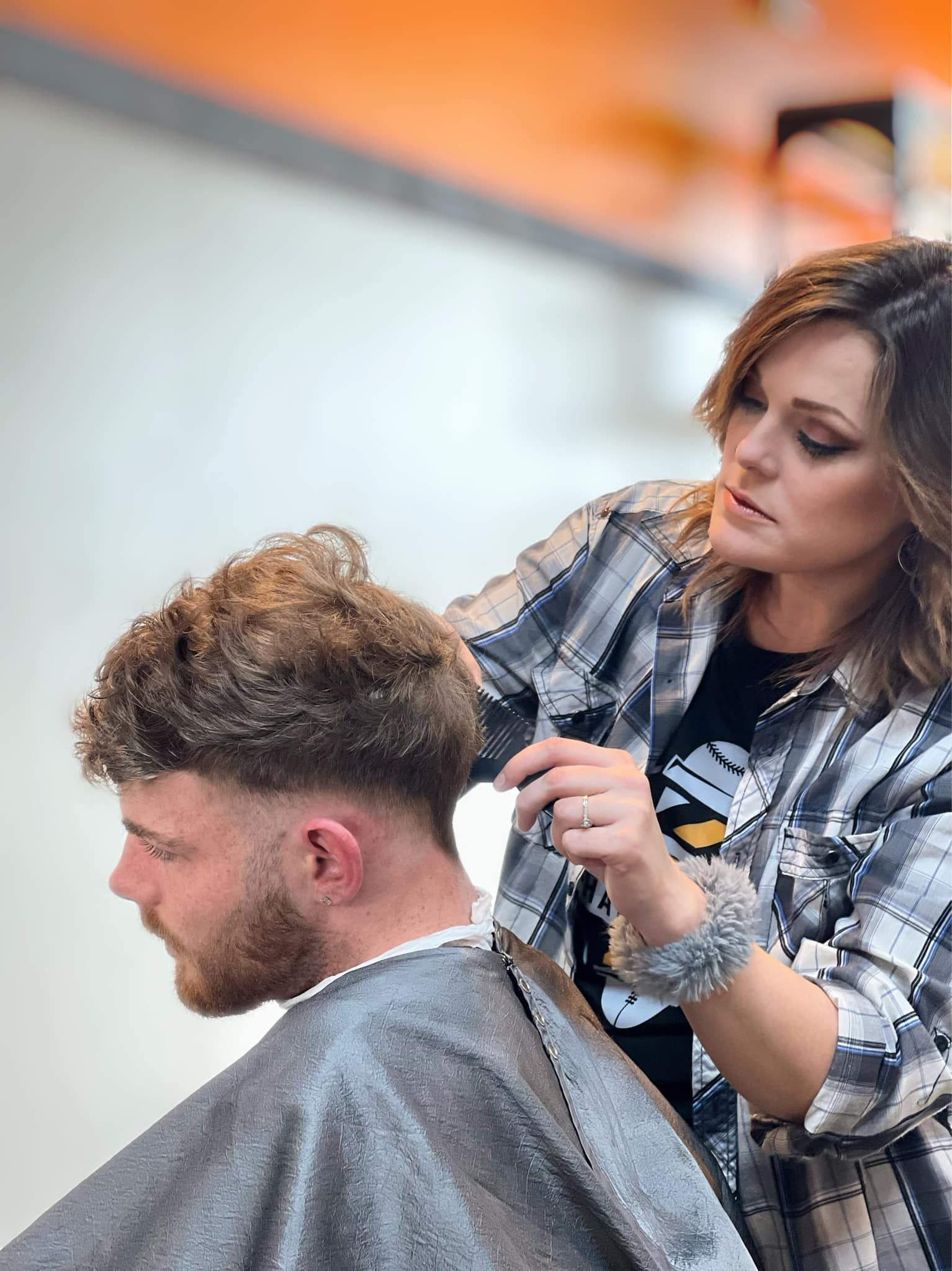 Stylist trimming a man's hair in a salon, with clippers and a cape.